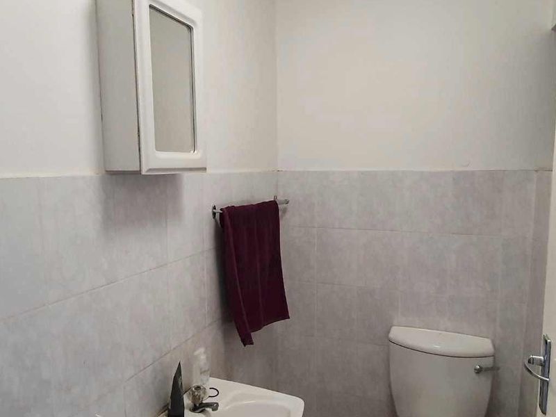 A compact bathroom featuring a wall-mounted medicine cabinet, ceramic washbasin, and standard toilet with partial wall tiling.