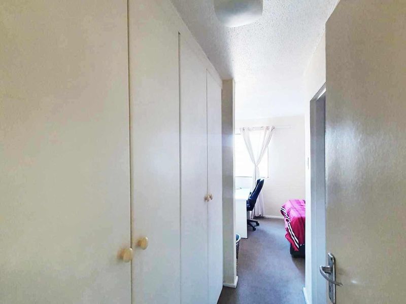 A functional hallway featuring built-in storage cupboards, leading into a bedroom area with natural light.