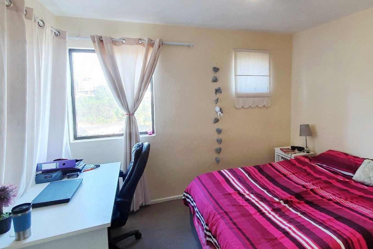 A functional bedroom featuring a window with a curtain rod and a fitted roman blind, providing natural light and ventilation.