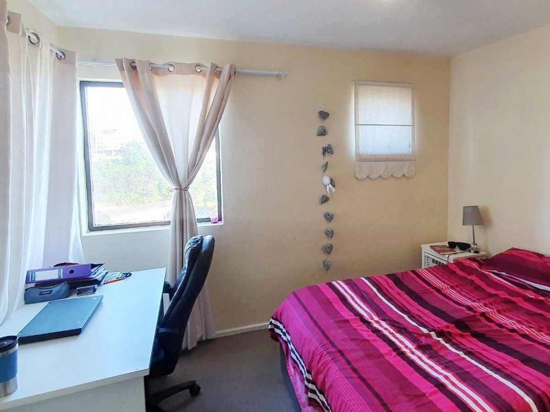 A functional bedroom featuring a window with a curtain rod and a fitted roman blind, providing natural light and ventilation.