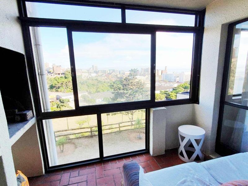 Enclosed balcony featuring a built-in braai, tiled flooring, and large windows offering expansive city and landscape views.