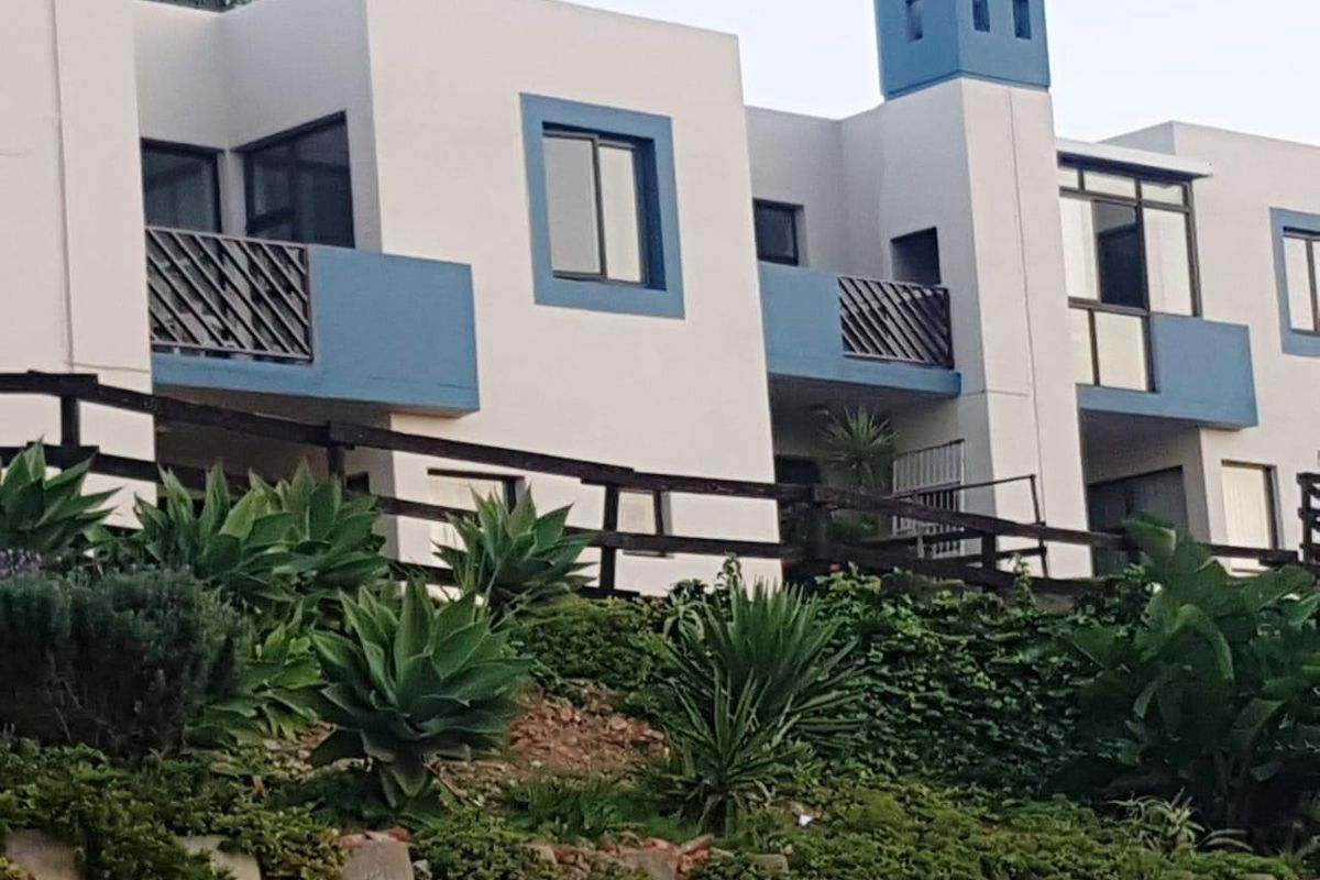 Rear elevation of a multi-level apartment complex featuring private balconies with metal railings and a prominent chimney stack.