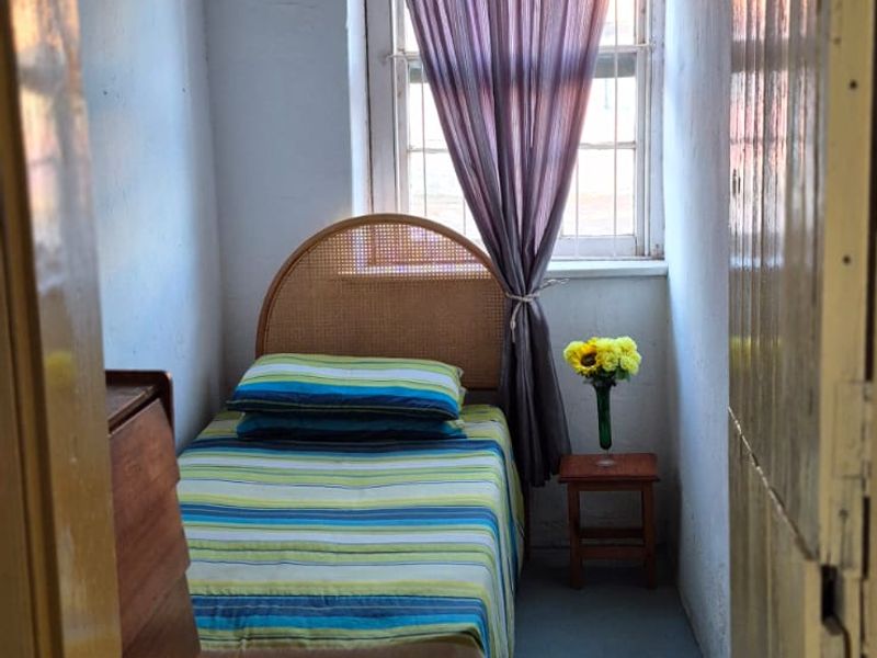A compact bedroom featuring a window with natural light and a painted concrete floor, offering a simple and functional living space.