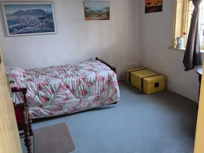 A simple bedroom featuring a timber ceiling and a window, with painted concrete flooring and plain wall finishes.