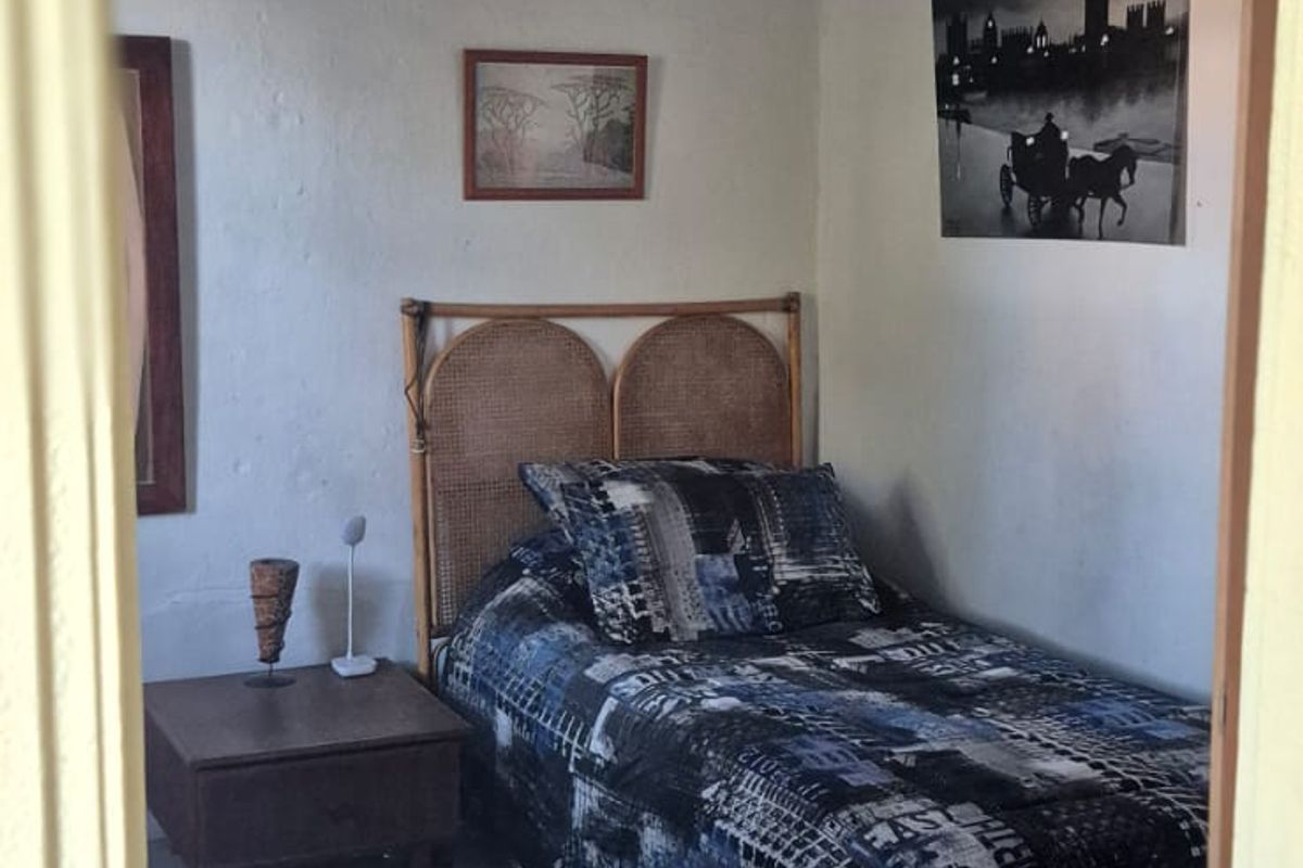 A simple bedroom featuring a single bed, neutral walls, and a dark wood ceiling, offering a basic living space.