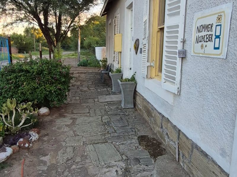 A rustic exterior walkway featuring stone paving, traditional louvred window shutters, and stone foundation detailing along the side of the property.