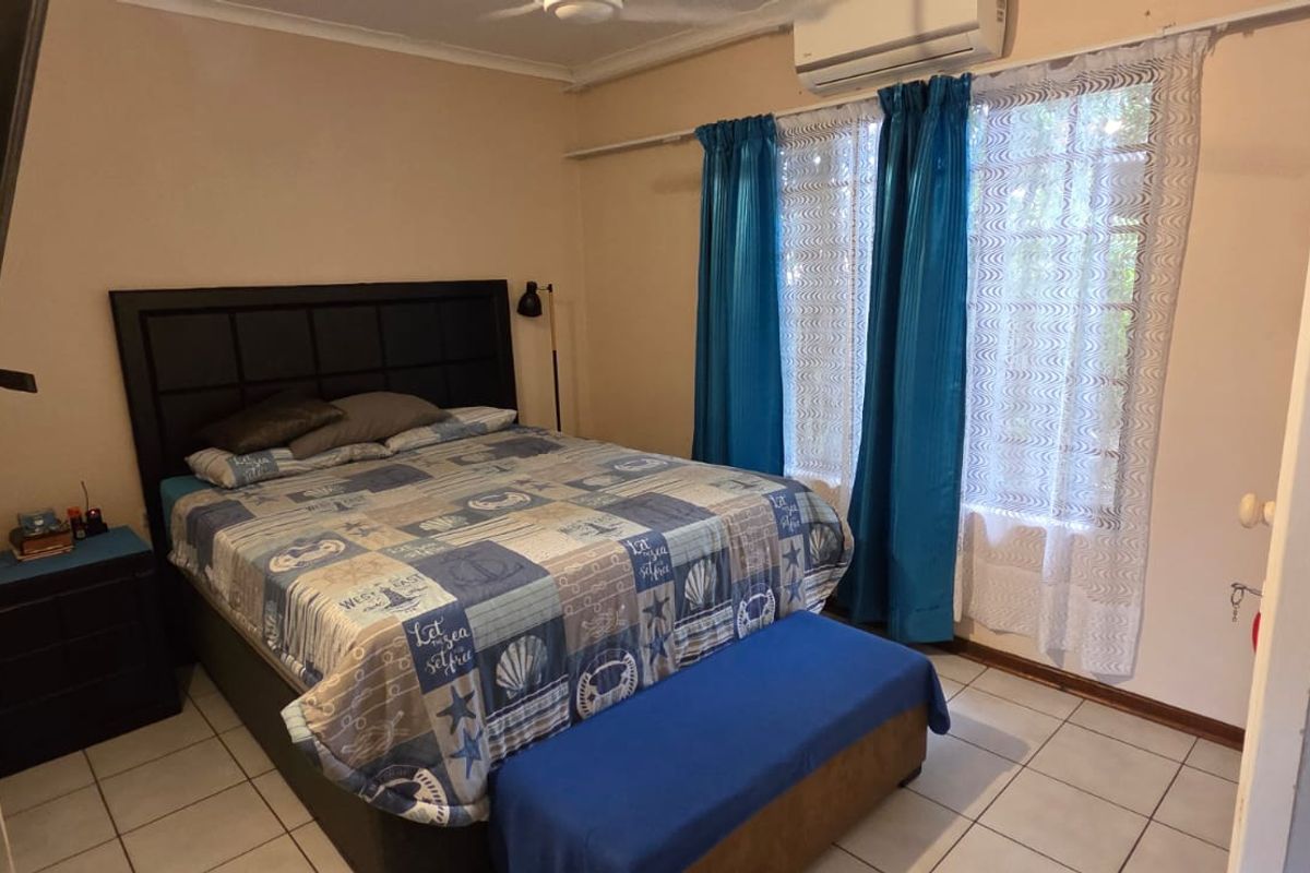 A functional bedroom featuring tiled flooring, a ceiling fan, and a wall-mounted split-system air conditioning unit.