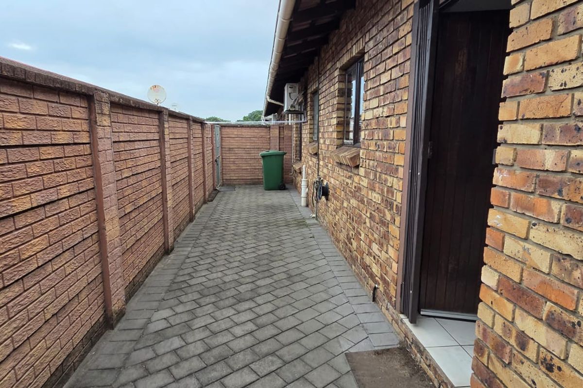 A side exterior walkway featuring face brick walls and paved flooring, providing access to the rear of the townhouse property.