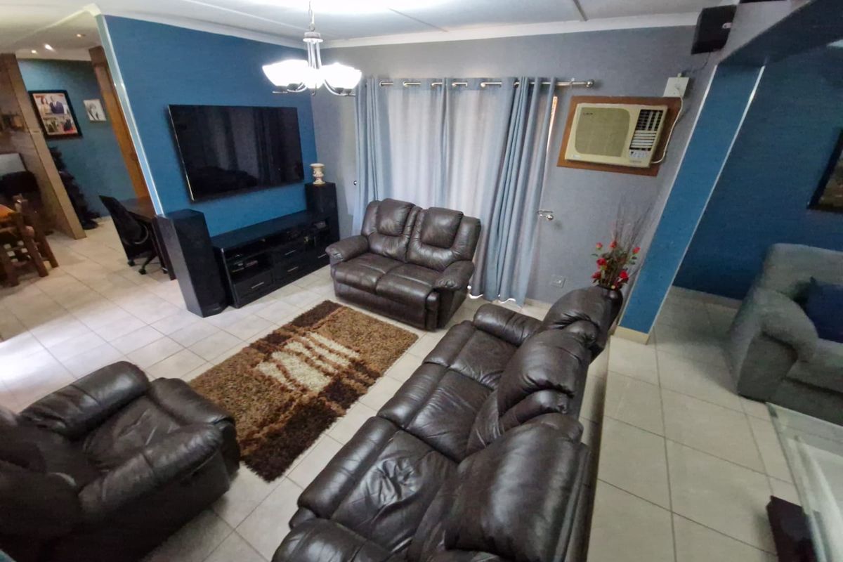 A spacious living room featuring tiled flooring, blue accent walls, and a built-in wall-mounted air conditioning unit.