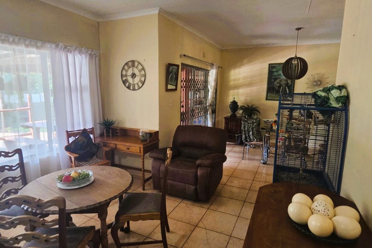 A living area featuring tiled flooring, coved ceilings, and large windows providing natural light and a view of the outdoor pool area.
