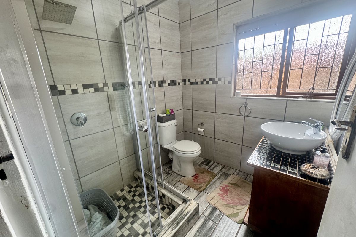 A functional bathroom featuring a glass-enclosed shower, a modern vessel sink on a vanity, and a toilet, finished with neutral wall and floor tiling.