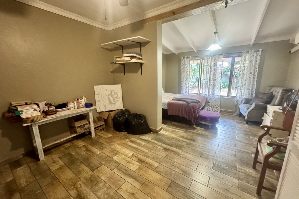 A spacious bedroom featuring wood-look tile flooring, crown molding, and a semi-open layout with natural light from the rear window.