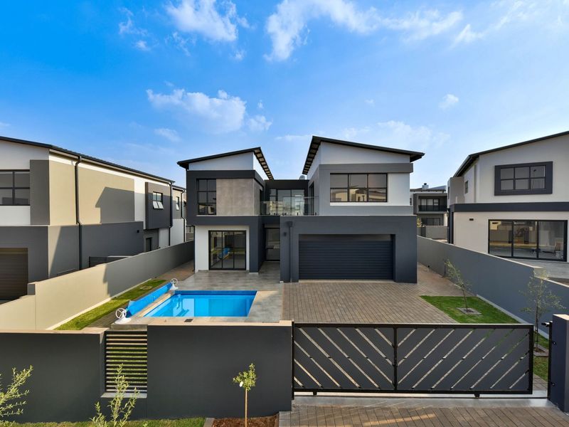 Modern double-story residential property featuring a paved driveway, double garage, swimming pool, and contemporary architectural design with clean lines.