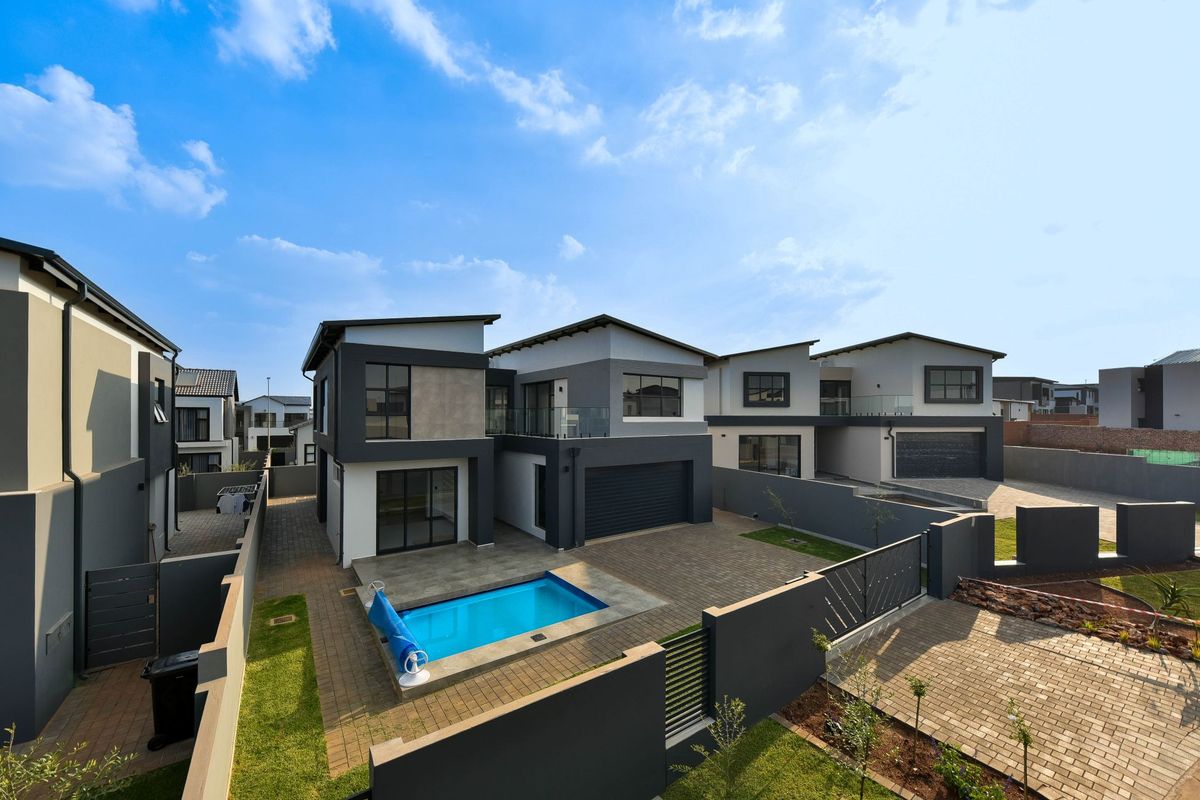 Rear view of a modern double-story house featuring a paved courtyard, private swimming pool, secure boundary walls, and an integrated garage.