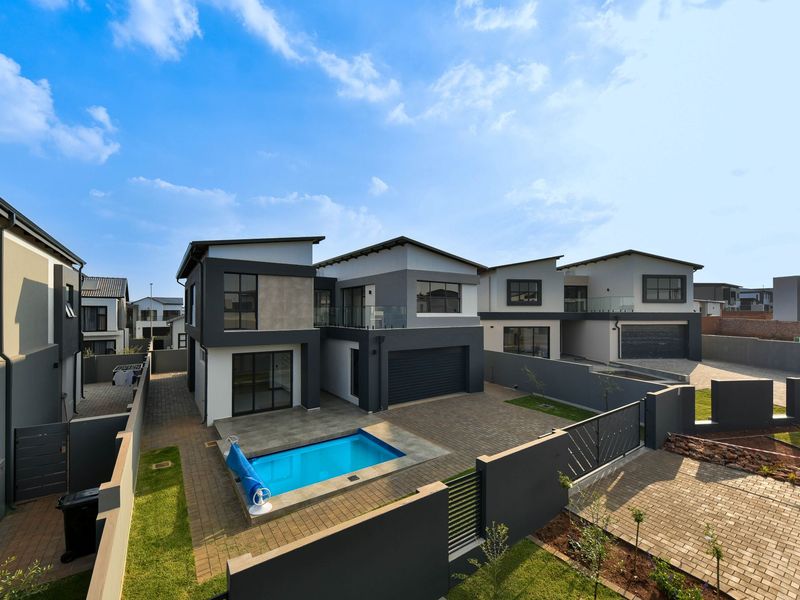 Rear view of a modern double-story house featuring a paved courtyard, private swimming pool, secure boundary walls, and an integrated garage.