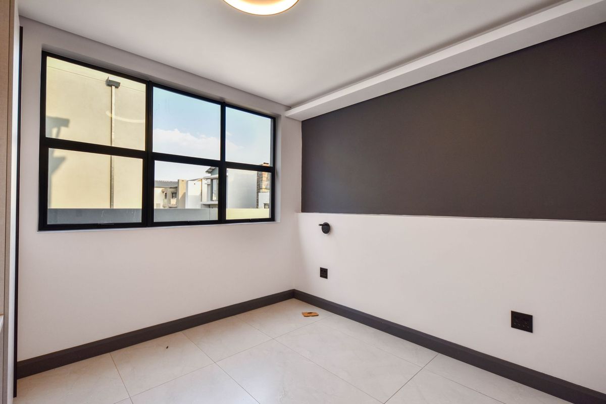 A bright, modern, and empty bedroom featuring large black-framed windows, neutral tiled flooring, and a contemporary two-tone wall finish.