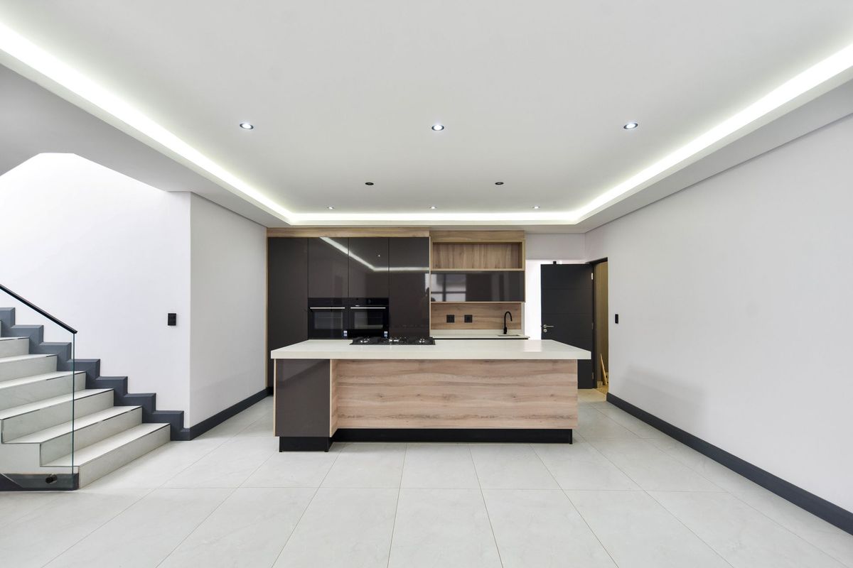 Modern open-plan kitchen featuring a central island, built-in appliances, sleek cabinetry, and recessed ceiling lighting, adjacent to a contemporary staircase.