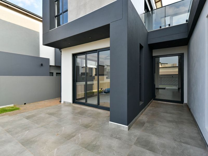 A modern covered patio area featuring large format floor tiles, sliding glass doors, and a sleek glass balustrade on the upper level.