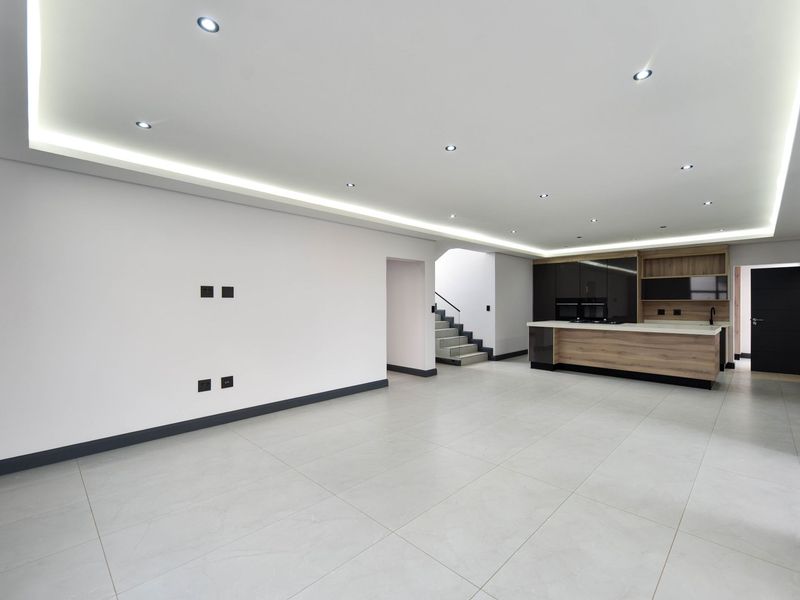 Spacious open-plan living and kitchen area featuring modern tiled floors, recessed cove lighting, and a contemporary kitchen island with built-in cabinetry.