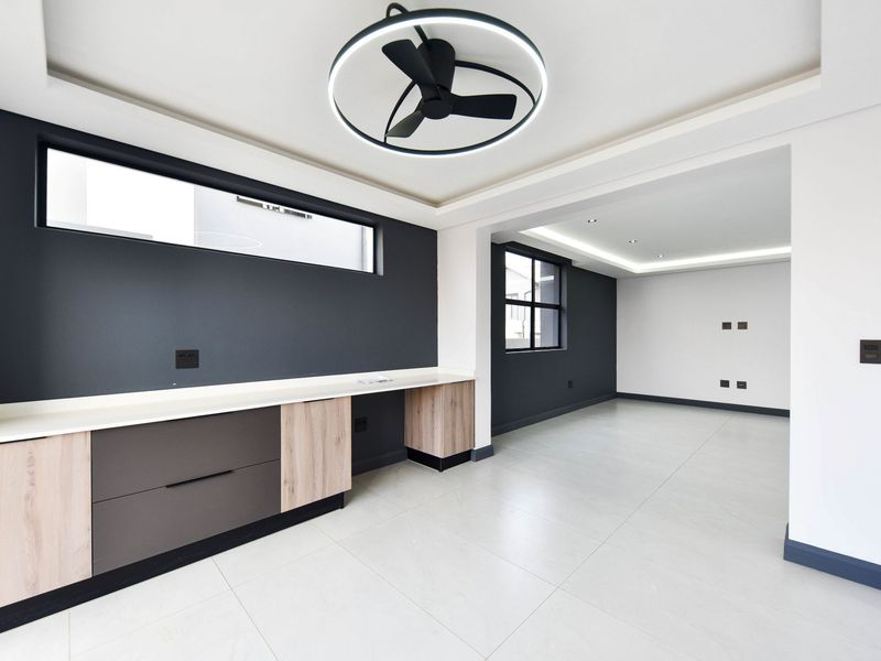 Modern, open-plan living area featuring sleek built-in cabinetry, stone countertops, contemporary ceiling fan, and neutral tiled flooring with recessed lighting.