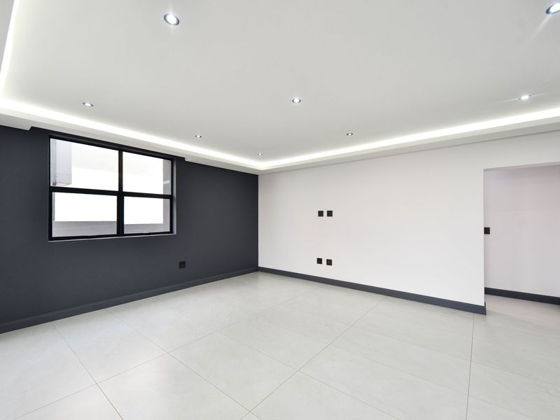 A modern, empty living room featuring neutral tiled flooring, contrasting dark and light wall finishes, recessed ceiling lighting, and cove lighting.