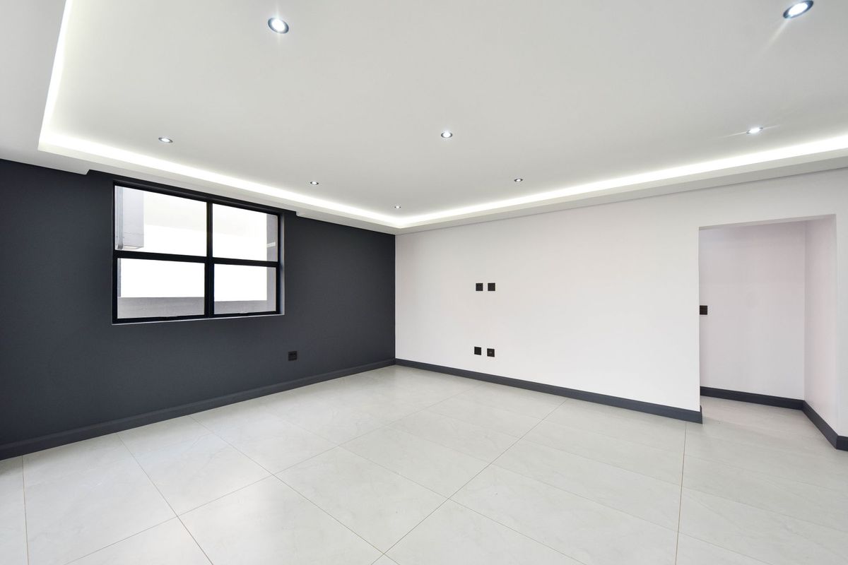 A modern, empty living room featuring neutral tiled flooring, contrasting dark and light wall finishes, recessed ceiling lighting, and cove lighting.