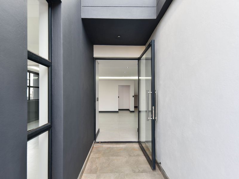 Modern entrance area featuring a sleek glass pivot door, contemporary dark exterior finishes, and clean, minimalist architectural lines leading into the home.