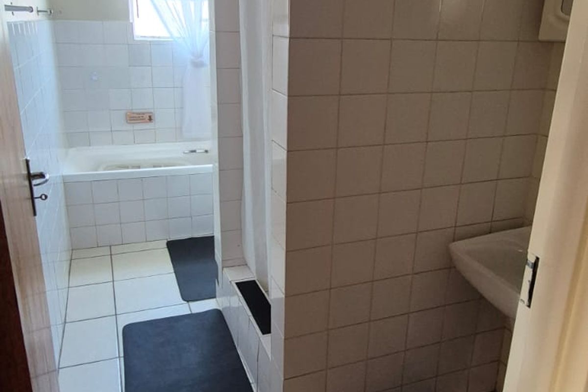 A functional bathroom featuring a tiled shower enclosure, a built-in bathtub, and a pedestal sink with neutral wall and floor tiling.