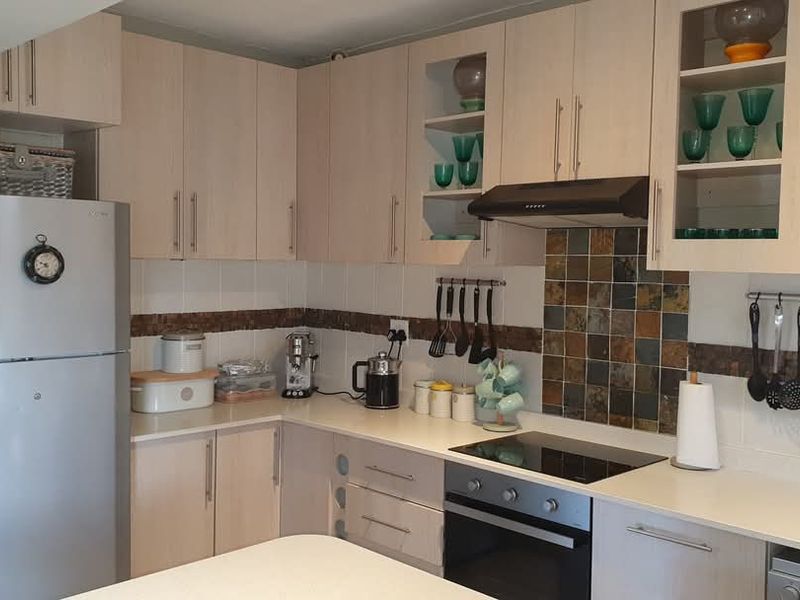 A functional kitchen featuring light wood-finish cabinetry, stone-look tiled backsplash, integrated electric hob, oven, and extractor fan with ample counter space.