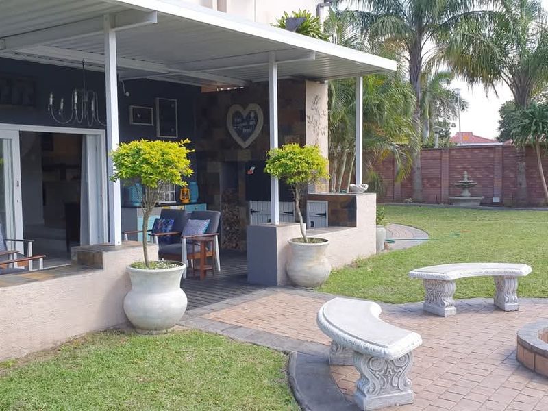 A spacious covered patio featuring a built-in braai, leading out to a landscaped garden with a paved fire pit area and stone benches.