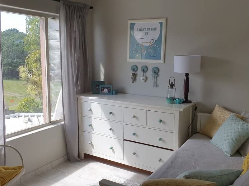 A bright bedroom featuring large windows that provide natural light and views of the surrounding greenery, complemented by neutral tiled flooring.