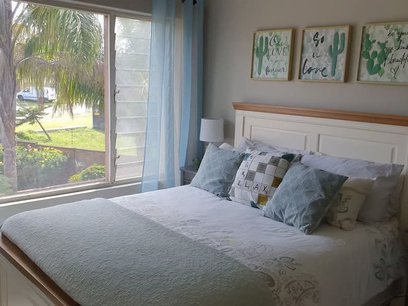 A cozy bedroom featuring large louvre windows that provide natural light and a view of the exterior garden area.