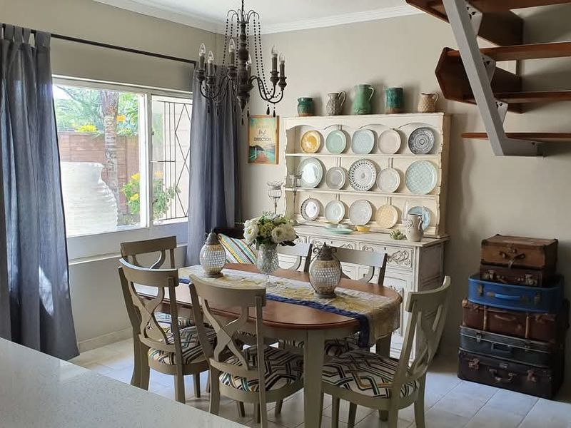 A well-lit dining area featuring tiled flooring, a decorative chandelier, and an open-tread staircase leading to the upper level.