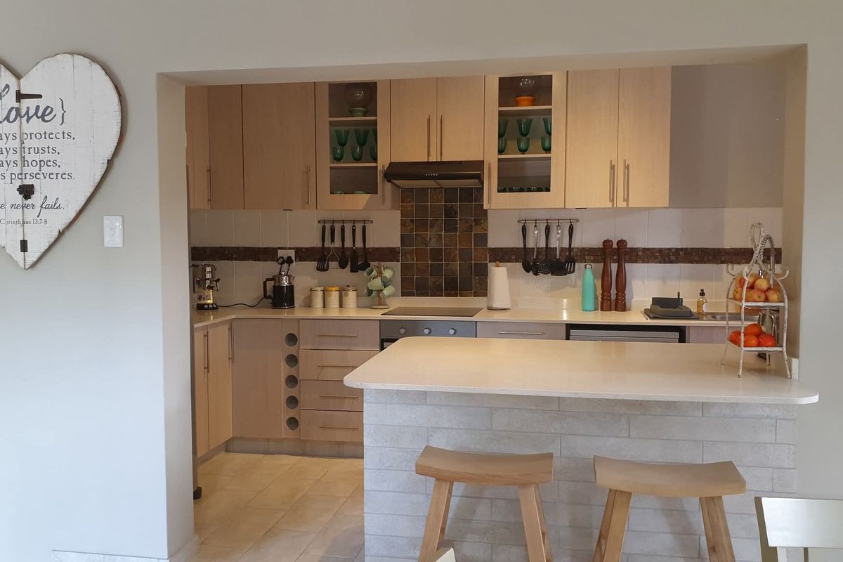 A functional kitchen featuring light wood cabinetry, stone countertops, a breakfast bar, and a tiled backsplash with integrated cooking appliances.