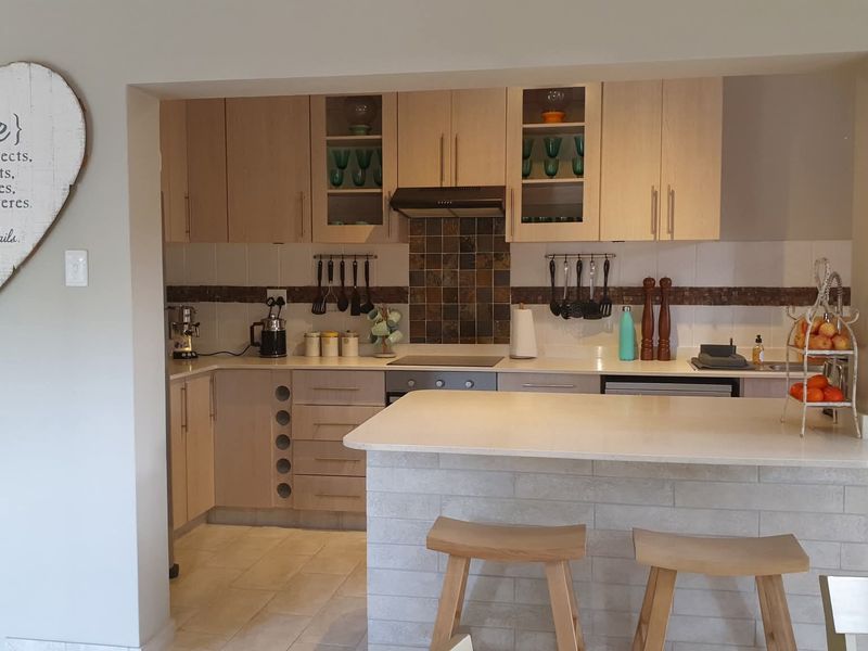 A functional kitchen featuring light wood cabinetry, stone countertops, a breakfast bar, and a tiled backsplash with integrated cooking appliances.