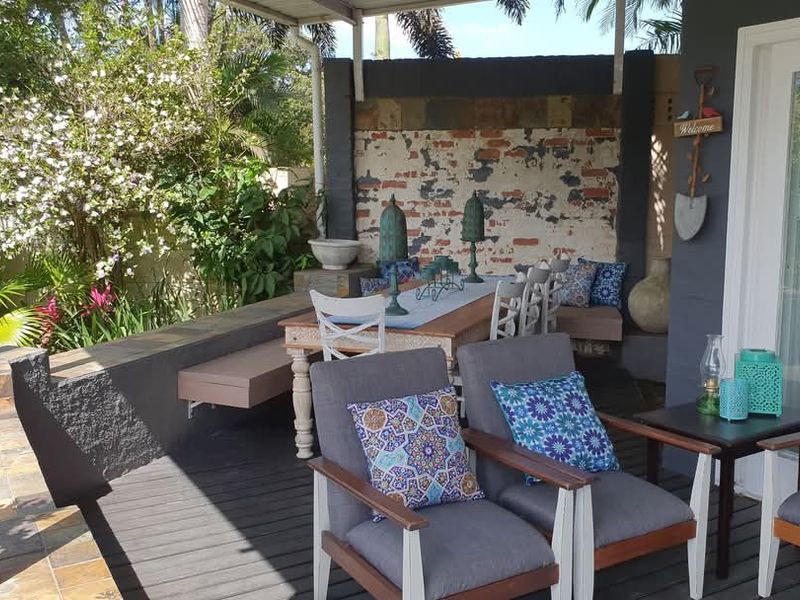 A covered outdoor patio area featuring timber decking, built-in bench seating, and a decorative brick feature wall, providing a comfortable space for outdoor entertaining.
