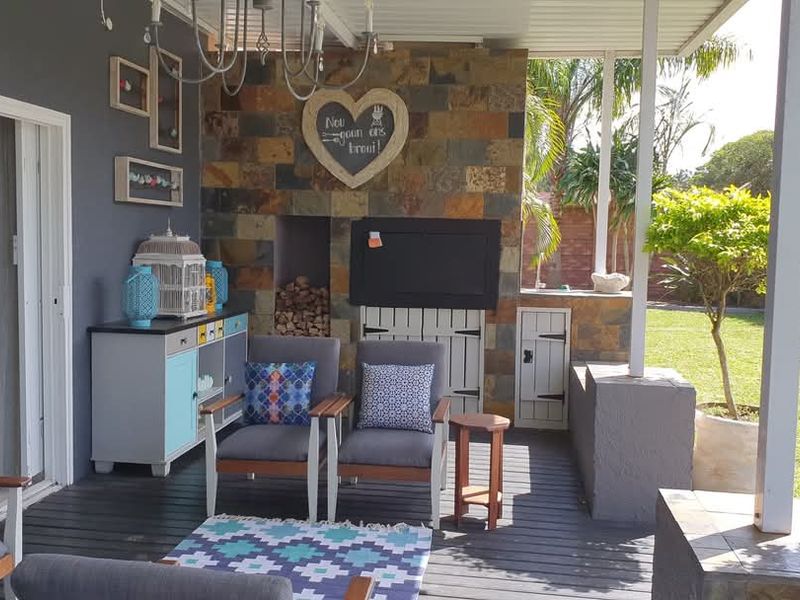 Covered patio featuring a built-in braai with stone cladding, wooden decking, and direct access to the garden through sliding doors.