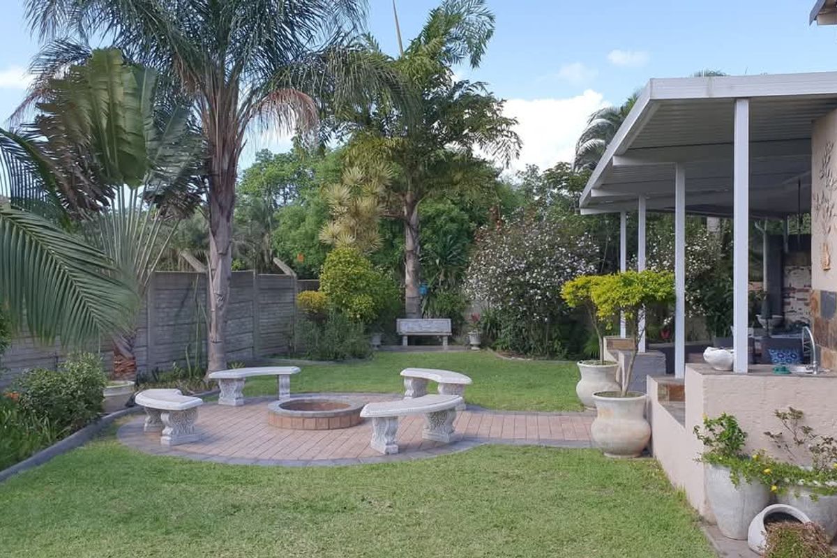 A well-maintained rear garden featuring a covered patio, built-in braai area, and a paved fire pit circle, perfect for outdoor entertaining.