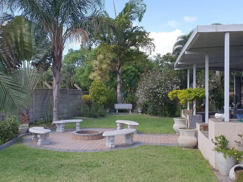 A well-maintained rear garden featuring a covered patio, built-in braai area, and a paved fire pit circle, perfect for outdoor entertaining.