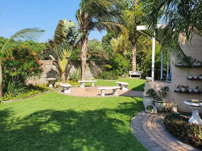 A well-maintained garden featuring a paved patio area with a built-in fire pit, concrete seating, and a covered outdoor space.