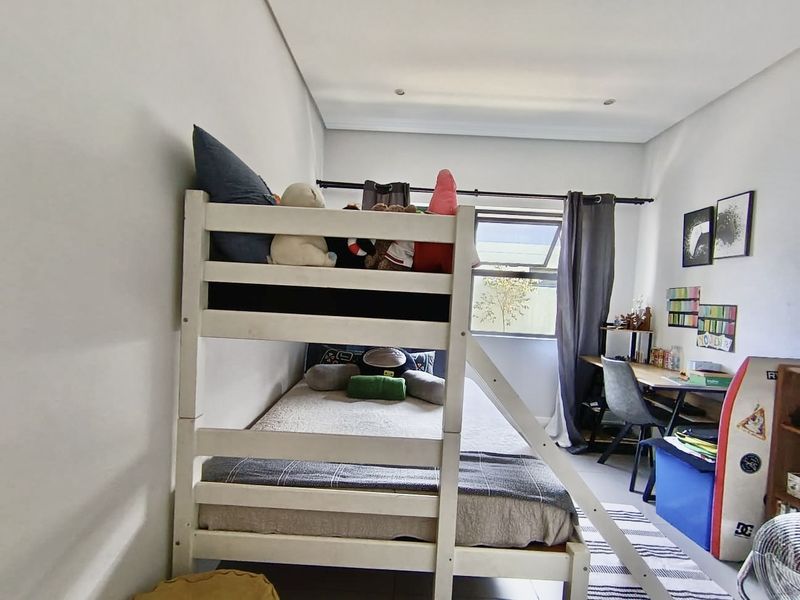 A functional bedroom featuring recessed downlighting and a top-hung window with curtain rod, providing natural light and a neutral backdrop.