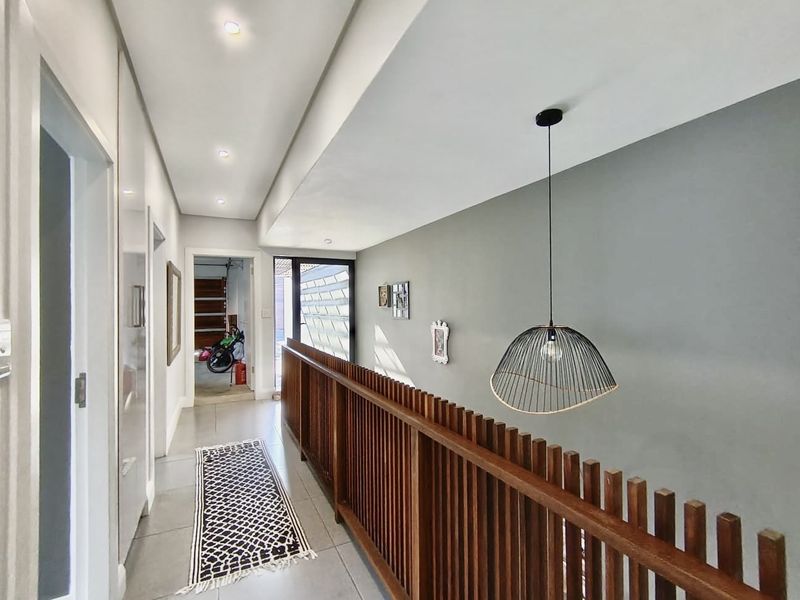 A bright, modern hallway featuring a timber slat balustrade, tiled flooring, and contemporary recessed and pendant lighting.