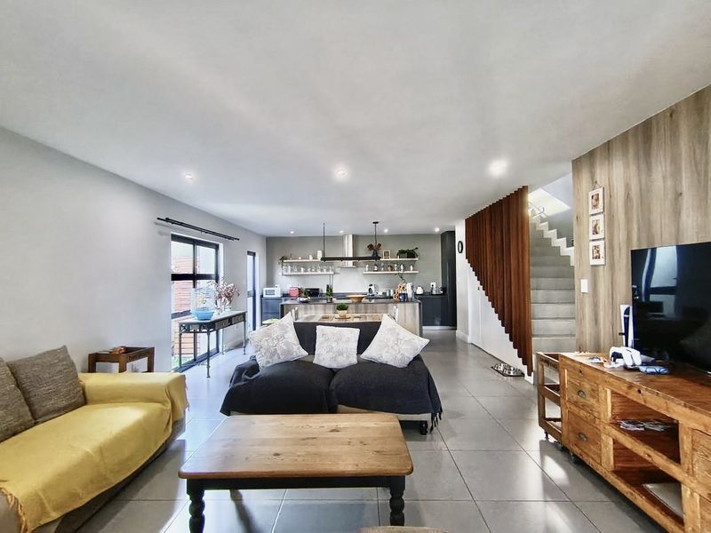 Spacious open-plan living area featuring a modern kitchen with island, tiled floors, and a distinctive timber slat staircase feature.