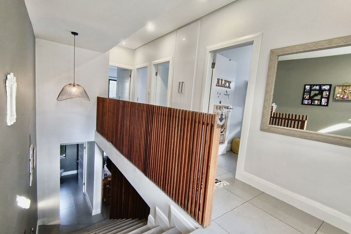 A bright upper-level hallway featuring a modern timber slat balustrade, tiled flooring, recessed lighting, and built-in storage cabinetry.