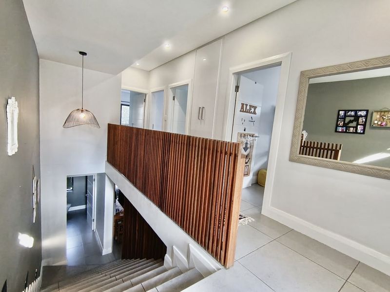 A bright upper-level hallway featuring a modern timber slat balustrade, tiled flooring, recessed lighting, and built-in storage cabinetry.
