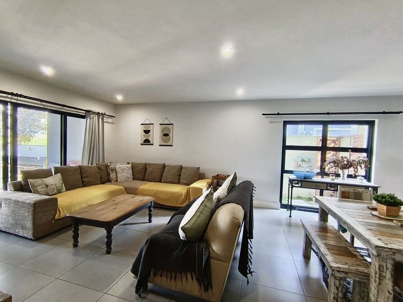 Spacious open-plan living and dining area featuring neutral tiled flooring, recessed downlights, and large black aluminium framed windows and sliding doors.