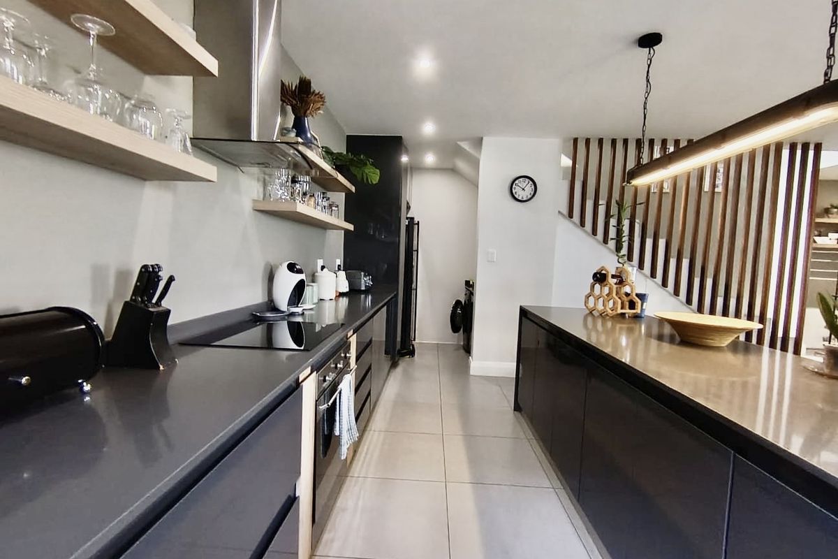 Modern kitchen featuring dark cabinetry, stone countertops, integrated appliances, floating shelving, and a stylish timber slat screen adjacent to the staircase.