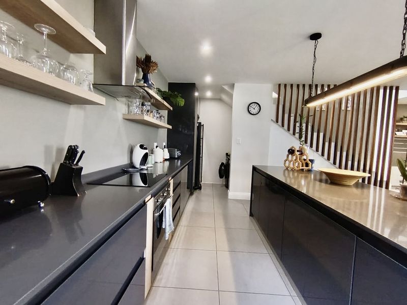 Modern kitchen featuring dark cabinetry, stone countertops, integrated appliances, floating shelving, and a stylish timber slat screen adjacent to the staircase.