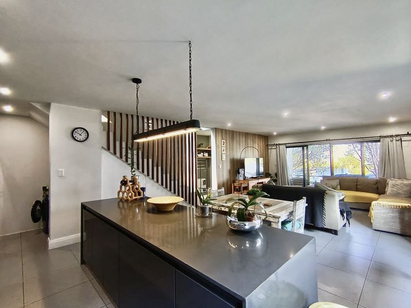 Spacious open-plan living area featuring a modern kitchen island, contemporary pendant lighting, and a distinctive timber slat staircase, flowing seamlessly to the outdoor space.