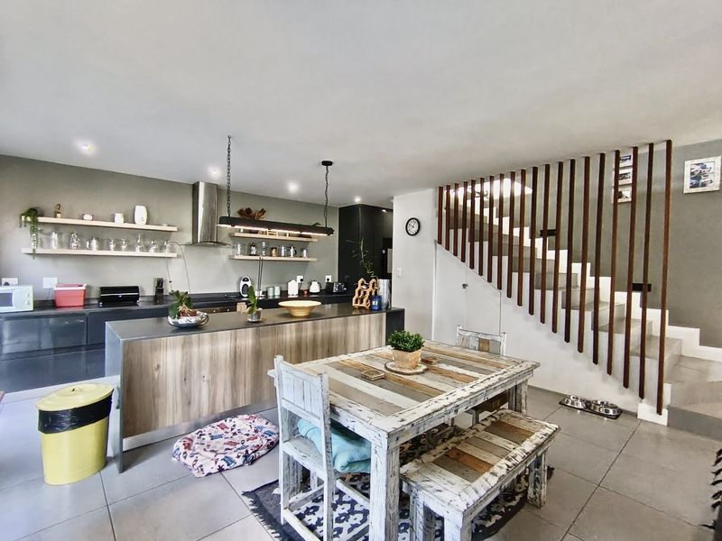 Modern open-plan kitchen and dining area featuring a central island, floating shelving, and a distinctive timber slat staircase balustrade.